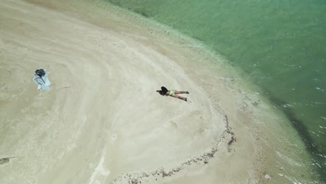 aerial view of a sexy girl in a thong bikini laying in the sand on a sandbar in the crystal clear waters of the tropical island of tobago