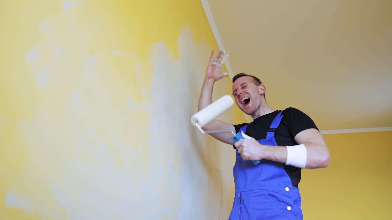 Man having fun during painting room. Professional young happy man with paint roller having fun