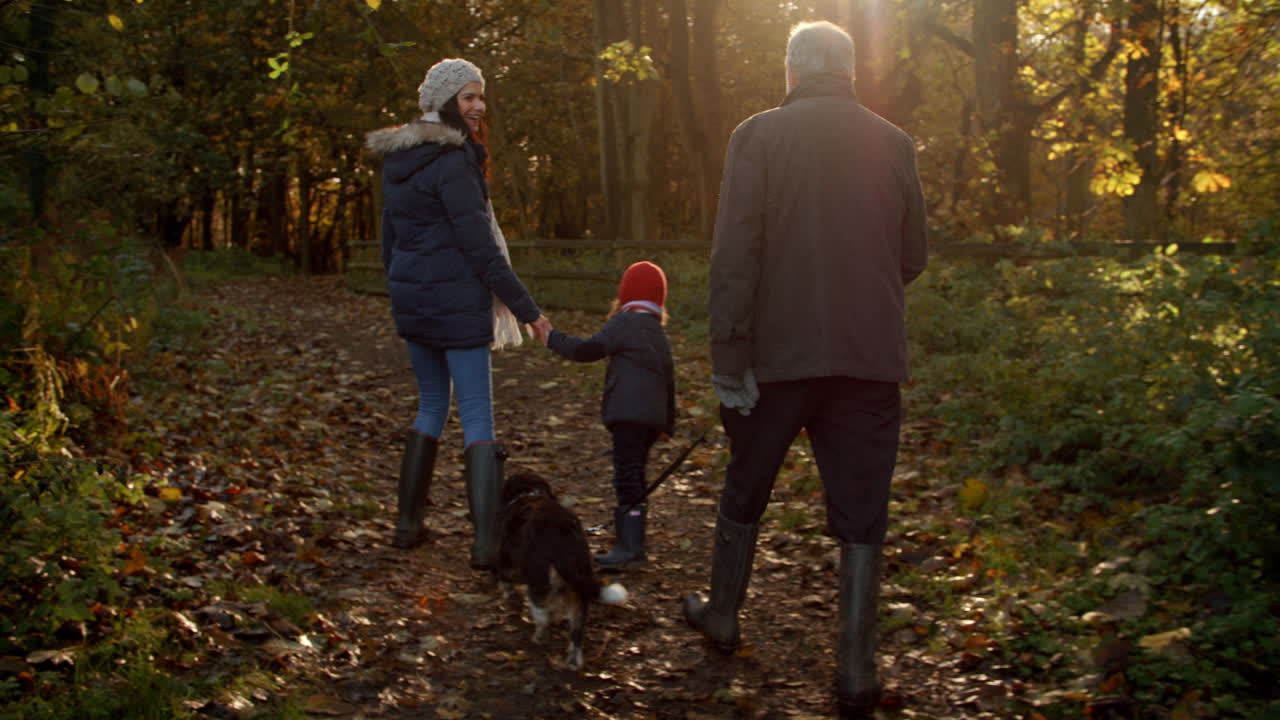 Familj med flera generationer tar med hund på promenad i höstlandskap.