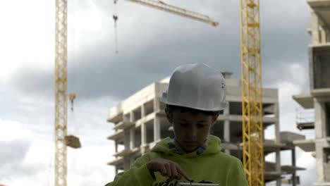 boy in a builder helmet plays a builder, controls the project on the tablet
