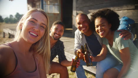 pov shot of friends on vacation sitting on porch of countryside cabin drinking beer and taking selfie