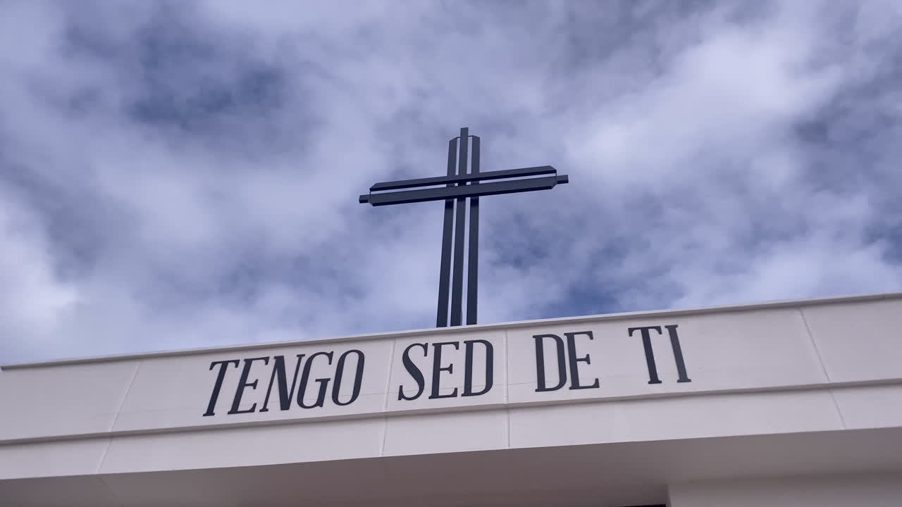 Modern cross standing on a building with the spiritual message I thirst for you against a cloudy blue sky