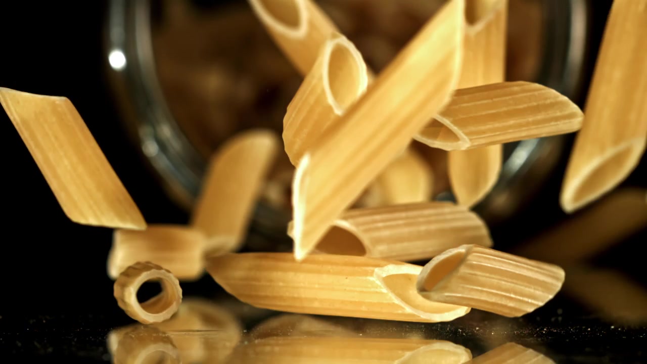 Penne crude che cadono al rallentatore su sfondo nero