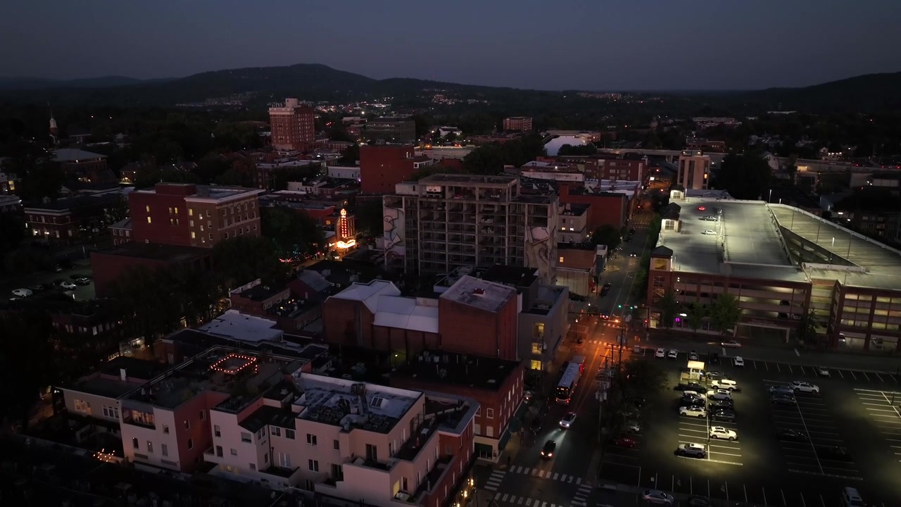 Ampia inquadratura in discesa di una città americana al crepuscolo. Via principale con traffico di notte. Zona residenziale con appartamenti e quartiere. Auto parcheggiate nel parcheggio