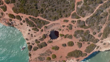 Drone-bird's-eye-view-rotate,-Benagil-cave-from-high-angle-showcasing-dirt-trails