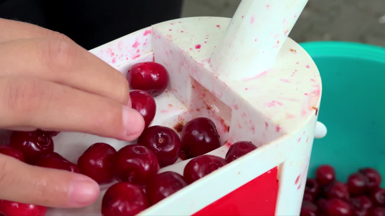 Cherry pitter, plastic tool and human hand inserting cherries in order to pit them, recorded at 120p, slowed down to 60p