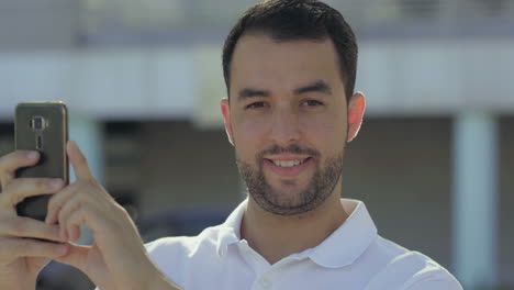 hombre caucásico sonriente tomando fotos con su teléfono inteligente.