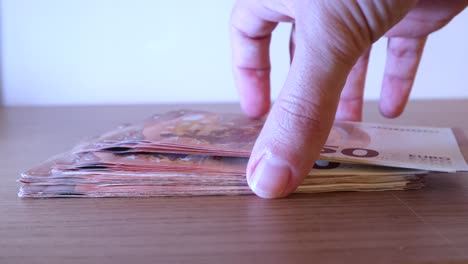 primer plano de manos masculinas tomando un montón de billetes de cincuenta euros de la mesa