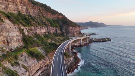 aerial footage of the sea cliff bridge, rising drone shot of the curving road above the blue waters of the pacific.