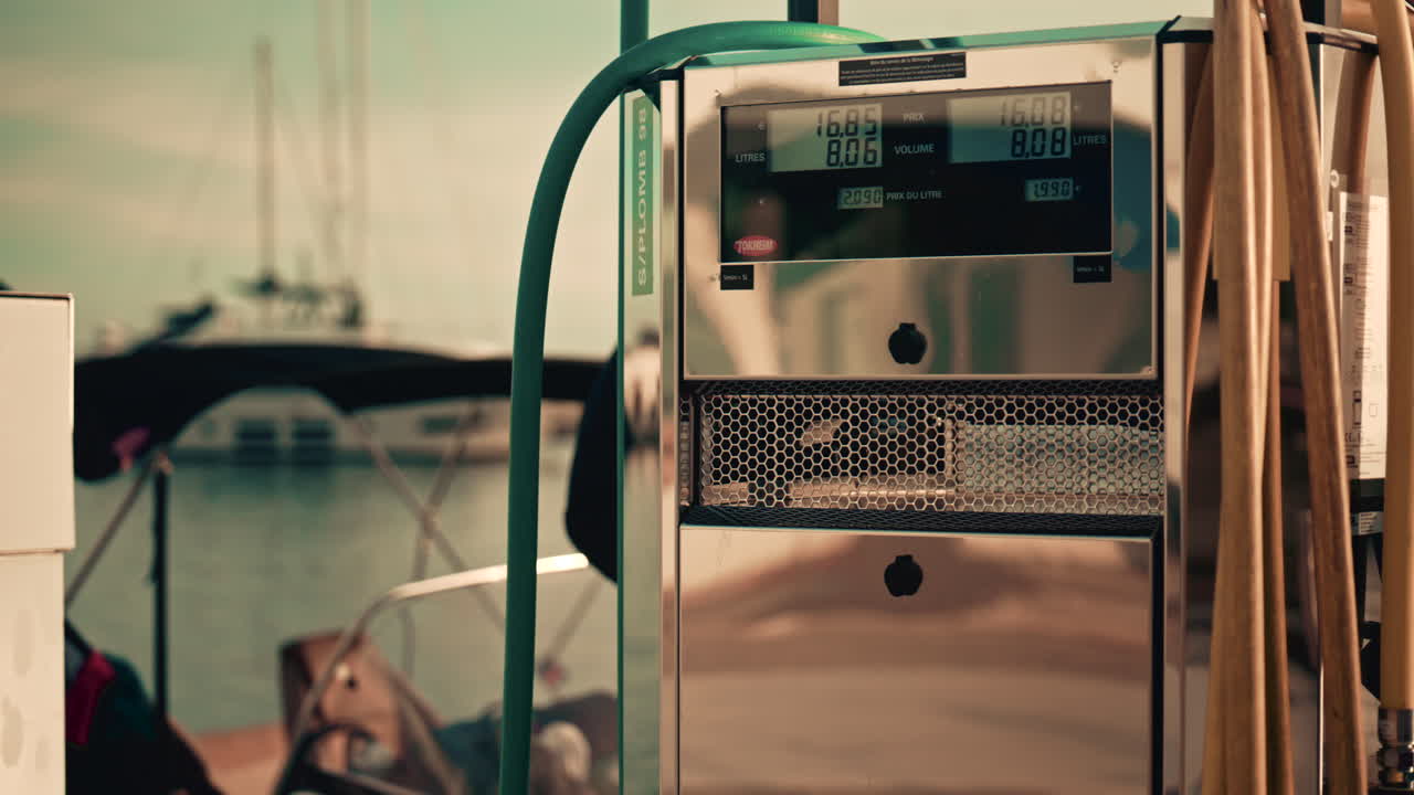Various hoses coloured in yellow, green, and blue, hang beside modern marina fuel pumps, boat at the fuel station