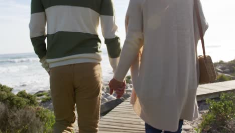 Caucasian-couple-enjoying-free-time-by-sea-on-sunny-day-walking-path