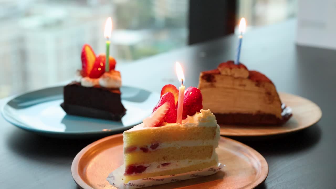 Three cakes with lit candles on plates, natural daylight, static camera, soft indoor ambiance