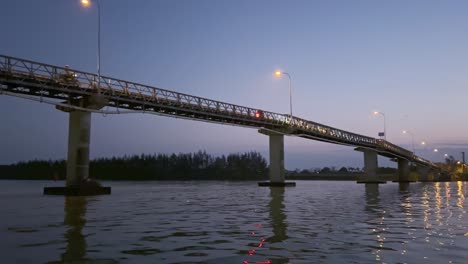 vehicles driving on cam kim bridge across thu bon river at sunset in hoi an, vietnam. wide shot