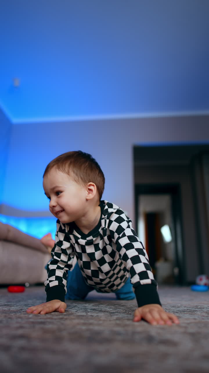 Cheerful Caucasian baby boy plays with rings from pyramid. Happy kid rolls the ring and stands up from the floor. Low angle view. Vertical video.