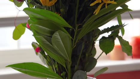 beautiful bouquet of flowers in rectangular glass vase sitting in water close up next to a sunny window sill on table, smooth pan down, store bought yellow, green, purple, and orange