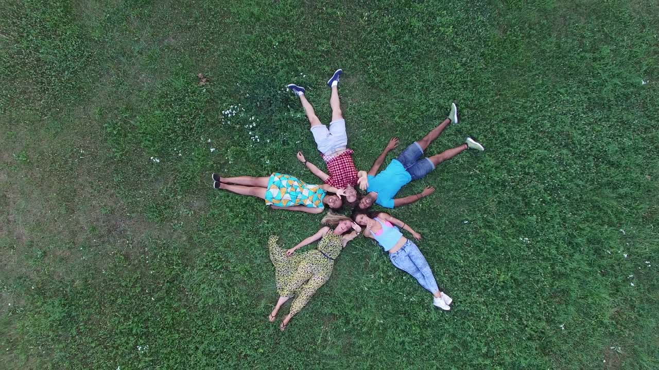 젊은 친구들이 잔디에 누워서 카메라를 향해 손을 흔들며 별 모양을 하고 있습니다.