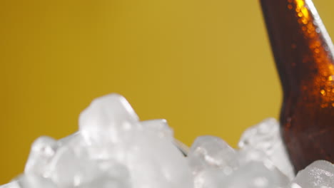 close up de una persona que toma una botella de vidrio refrigerada de cerveza fría o refrescos de un cubo lleno de hielo contra un fondo amarillo