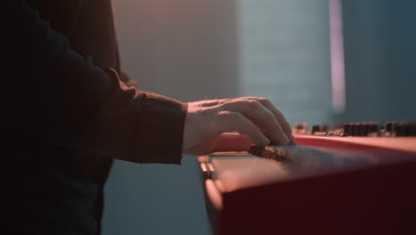 closer side view of a keyboardist's hand playing a red sampler piano. the detailed shot highlights the musician's precise finger movements on the keys