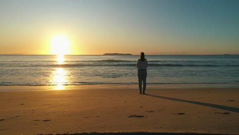 woman silhouette stands alone at the beach contemplating the ocean