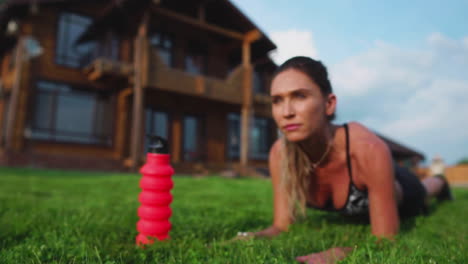 Hermosa-Morena-En-El-Fondo-De-Una-Gran-Mansión-Dedicada-Al-Fitness-Y-Realiza-Ejercicios-De-Plancha-Para-La-Prensa,-Entrenando-Al-Aire-Libre