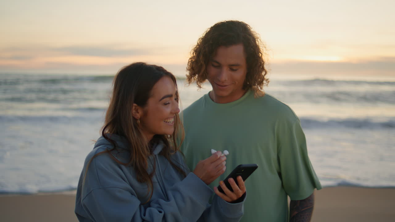 adolescentes relajados mirando el teléfono en el océano de la noche. amores escuchando música