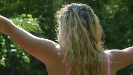 young woman raises her hands to the sky, sun shines through her fingers