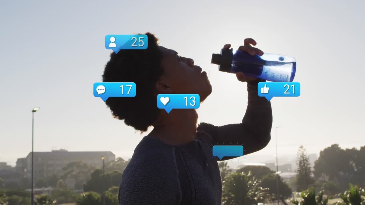animación de iconos de notificación y números sobre hombre afroamericano bebiendo agua contra el cielo