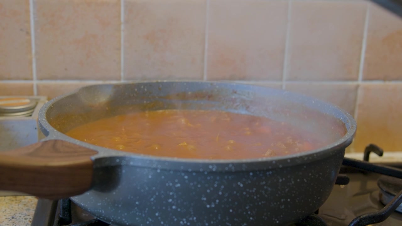 Coperchio sollevato da una pentola di chili sul fornello che rilascia una nuvola di vapore, cucina di casa.