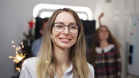 Young-businesswoman-at-a-company-party-holding-a-sparkling-stick,-smiling-to-camera