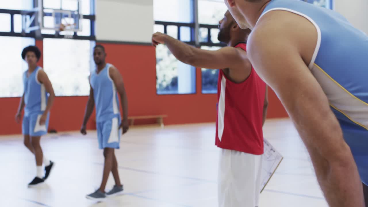 entrenador de baloncesto masculino diverso instruyendo el entrenamiento del equipo en la cancha cubierta, en cámara lenta