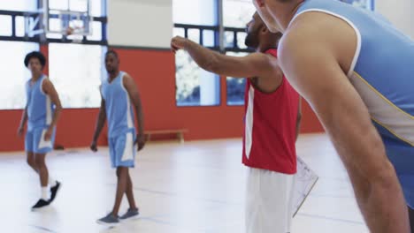 diverse male basketball coach instructing team training at indoor court, in slow motion