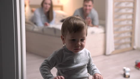 parents lying on the bed and their son is standing on the floor of the room