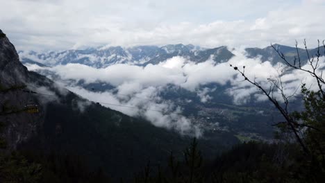 Vistas-Escénicas-De-Los-Altos-Alpes-Alemanes-Hacia-El-Valle-Con-Un-Teleférico-Que-Pasa-De-Izquierda-A-Derecha,-Trayendo-A-Los-Turistas-De-Regreso-Al-Valle,-Muchas-Nubes-En-El-Fondo