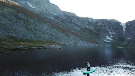 young woman on paddle board in alpine lake under mount evans byway