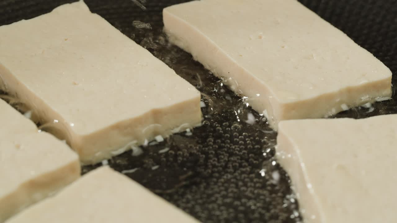 Fried tofu with sesame seeds and spices on cast iron pan, cooking japanese salad. Healthy ingredient for cooking vegan vegetarian diet food. Roasted tofu over black background.