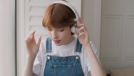 vista de cerca de una chica sentada en el alféizar de la ventana, luego se pone los auriculares y toca música desde su smartphone