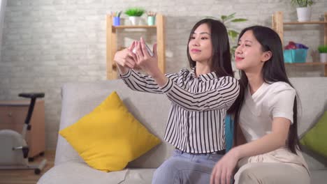 two happy young asian girls taking selfie sitting on the couch