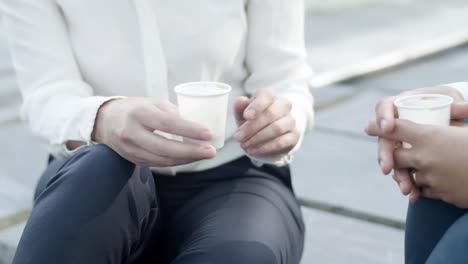 앉아서 테이크 아웃 커피를 마시고 말하고 몸짓을하는 여성 사무실 동료