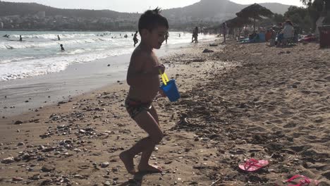 caucasian toddler running out of sea , holding a toy bucket on his hand