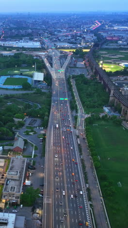 speed motorway with lots of transport passing by. drone footage over the city with green parks, rivers and stadiums. new york at sun down. vertical video
