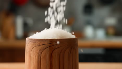 rice being poured into a wooden container in a kitchen setting