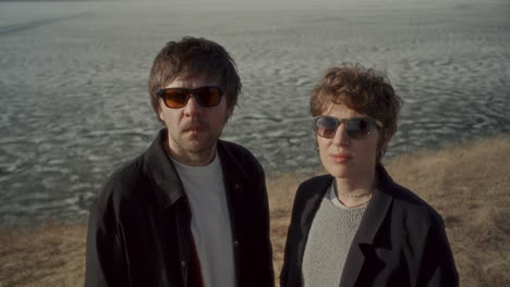 portrait of stylish couple in sunglasses by frozen lake