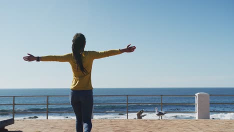 african american woman walking with arms outstretched on promenade by the sea