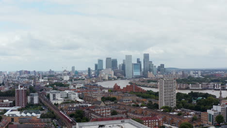 Ascending-footage-of-tall-apartment-house.-Revealing-panoramic-view-of-town-with-Thames-river-and-Canary-Wharf-business-hub.-London,-UK