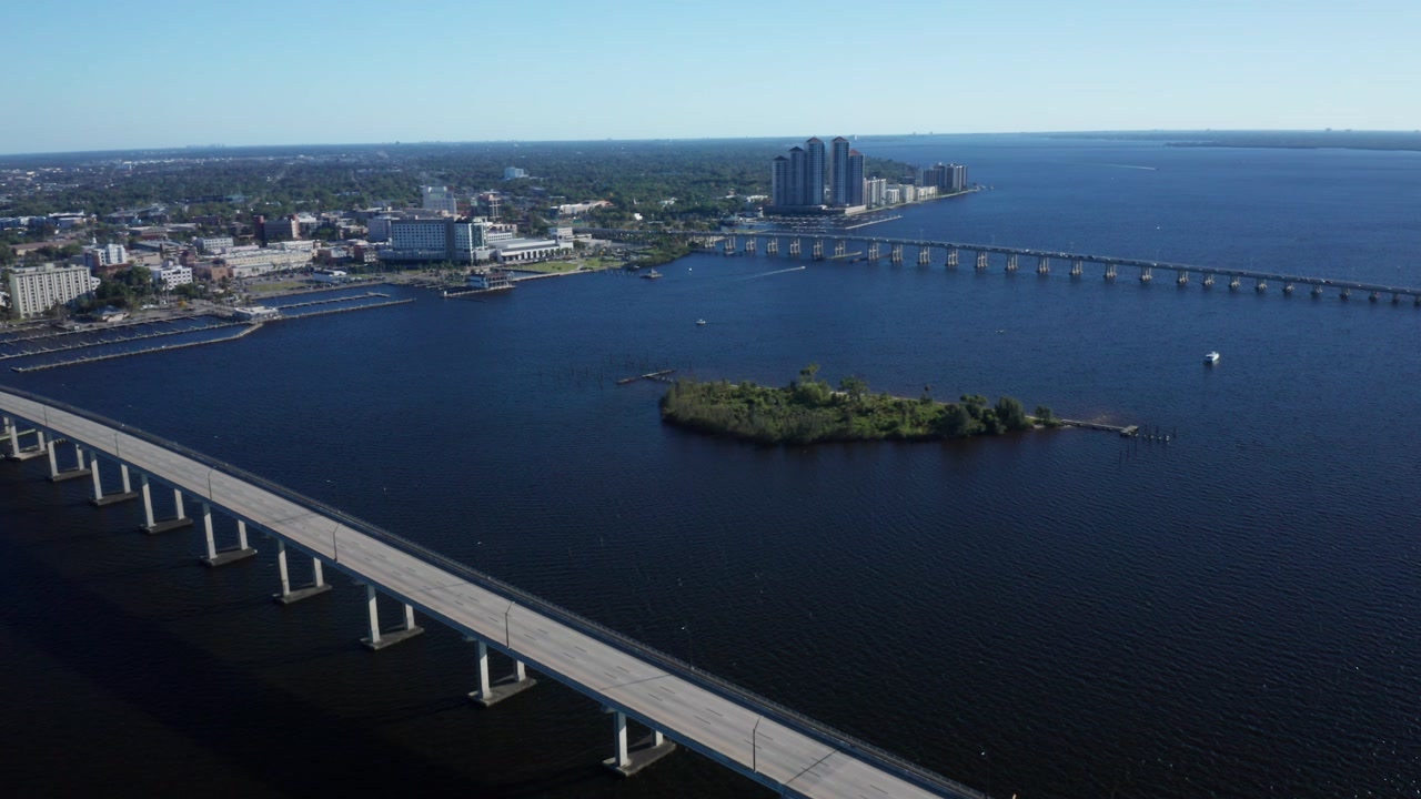 A bridge spans across the Caloosahatchee River, leading towards the Fort Myers skyline with high-rise buildings. Ideal for use in travel commercials or cityscape features.