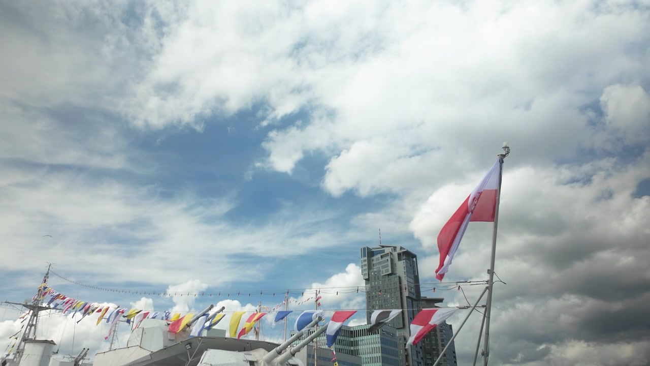 Una bandiera nazionale polacca bianca e rossa sventola al vento sul ponte di una nave a Gdynia, con architettura moderna e un cielo nuvoloso. Autentica atmosfera di viaggio e marittima