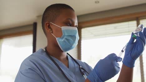 african american female doctor wearing face mask preparing covid vaccine for patient