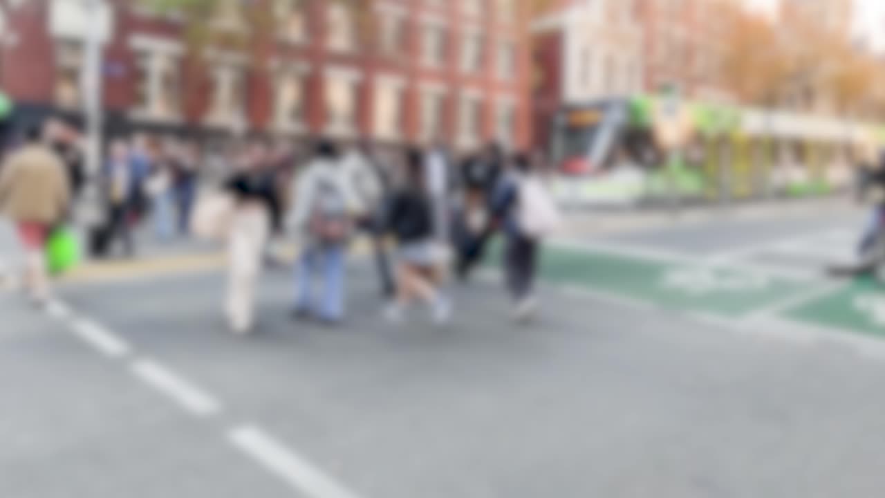Crowds cross a bustling city street in Melbourne, Australia, under daylight with blurred motion capturing dynamic movement