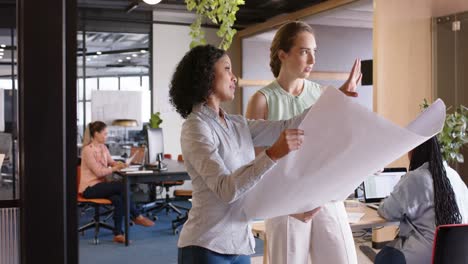 diversas arquitectas discutiendo el trabajo y mirando planos en la oficina, en cámara lenta