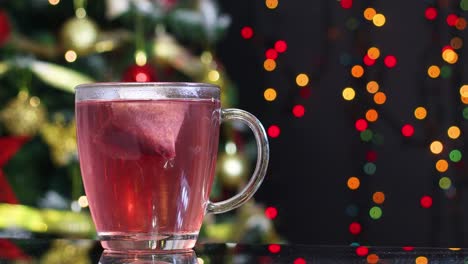 té caliente en la mesa y luces parpadeantes en el árbol de navidad detrás